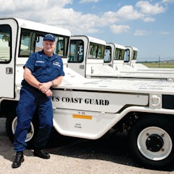 Chief Warrant Officer Greg McDermott stands in front of a new fleet of SATS, a standardized tow tractor developed originally for the United States Army.