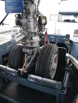 Two major components of the Taxibot make it different from other towbarless tractors: An interface mechanism clamps on the nose landing gear, which is in turn mounted on a “rotating turret.' Two major components of the Taxibot make it different from other towbarless tractors: An interface mechanism clamps on the nose landing gear, which is in turn mounted on a “rotating turret.'