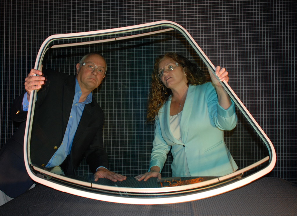 A pilot windshield made by PPG Industries for the new Dassault Falcon 5X business jet is looked over by project team members Nigel J. Thomas, segment manager, general aviation transparencies, and Veronica Frain, program manager, aerospace transparencies. The bird-resistant all-glass curved windshield has SURFACE SEAL(R) coating to enhance water shedding without wipers, and the heating system has been designed to meet challenging requirements including aesthetics and visibility. The windshields will afford expansive visibility.