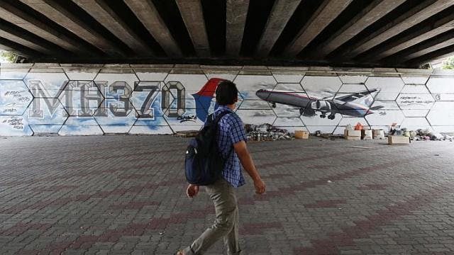 A man walks past graffiti depicting the missing Malaysia Airlines flight MH370 on the one year anniversary of its disappearance in Kuala Lumpur, on March 8, 2015.
