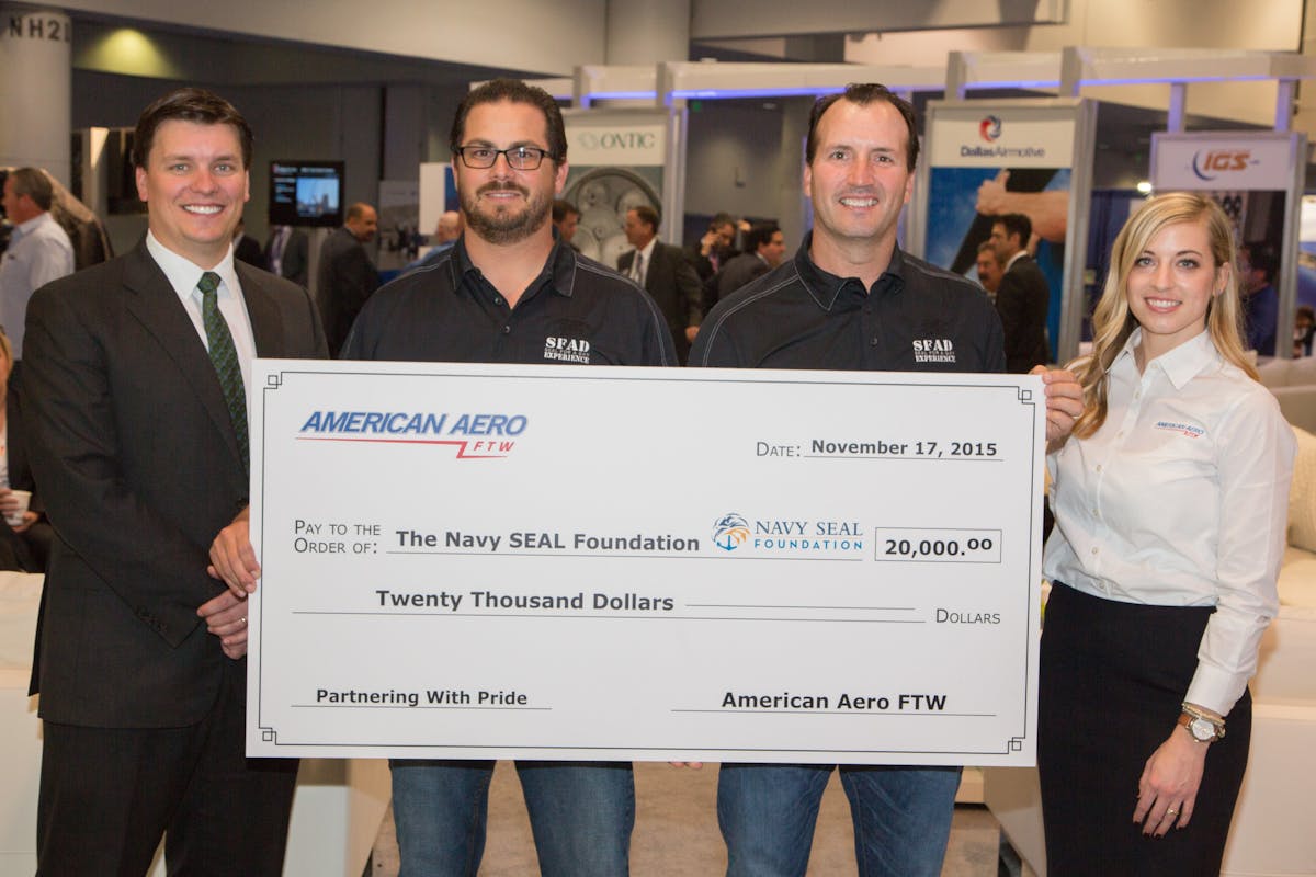 American Aero FTW, an FBO at Meacham International Airport in Fort Worth and a Signature Select FBO&trade;, donates $20,000 to support the Navy SEAL Foundation (NFS) at the NBAA 2015 Business Aviation Convention &amp; Exhibition in Las Vegas. From left to right, Riggs Brown, American Aero FTW General Manager; Carlo Franzia, former SEAL and founding member of SEAL Team 7 plank holder group; Mike Nemee, former SEAL; and Jackie Williamson, American Aero FTW staff member. Franzia and Nemee are volunteer ambassadors for the NSF and co-founders of the organization, SEAL FOR A DAY LLC. This organization provides NSF donors and corporate partners the opportunity to participate in team-building exercises and live-fire training with Navy SEALs at a private military training range in central California.