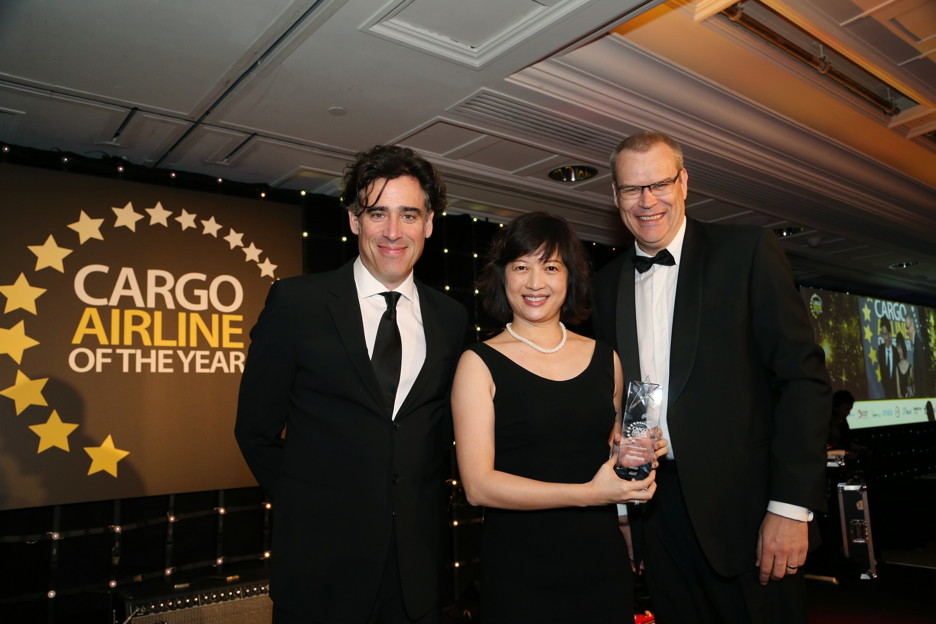 Vivien Lau accepts the award from Nick Platts, Head of Cargo, Heathrow Cargo (category sponsor, right), watched by well-known actor Stephen Mangan (left) who was the event&rsquo;s host.