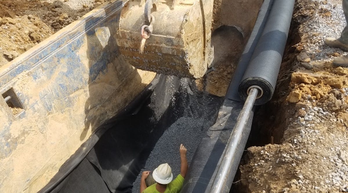 An initial layer of crushed stone bedding material was placed on top the geotextile, which was held in place on the side of the steel trench box with magnets.