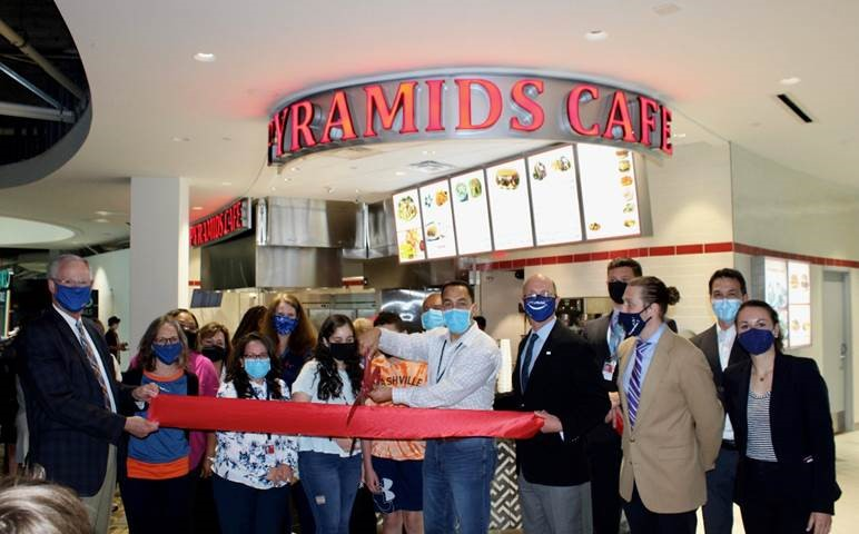 From left to right, Nashville International Airport President and CEO Doug Kreulen and Mike Mullaney, president and CEO of Fraport USA, hold the big red ribbon for George Hanna, surrounded by his family to celebrate the opening of Pyramids Caf&eacute; at BNA. Beloved in Nashville, Mr. Hanna&rsquo;s first airport location in Concourse C is now serving fliers fresh Mediterranean and Greek dishes.