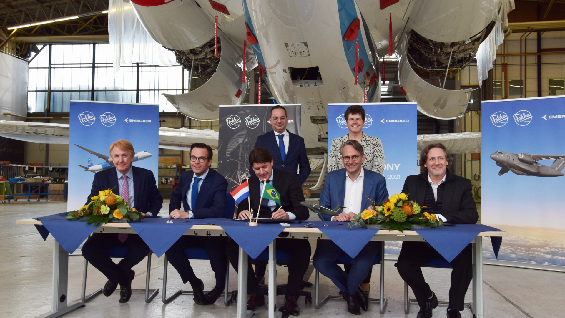 MoU signing ceremony on Oct. 18, 2021, at Fokker Techniek, in the Netherlands, witnessed by the mayor of Woensdrecht, Steven Adriaansen (standing left) and the governor of Noord Brabant, Ina Adema (standing right.) Seated (left to right): Jackson Schneider, president & CEO, Embraer Defense & Security; Arjan Meijer, president & CEO, Embraer Commercial Aviation; Menzo van der Beek, CEO of Fokker Services; Roland van Dijk, CEO of Fokker Techniek; and Johann Bordais, president & CEO, Embraer Services & Support.