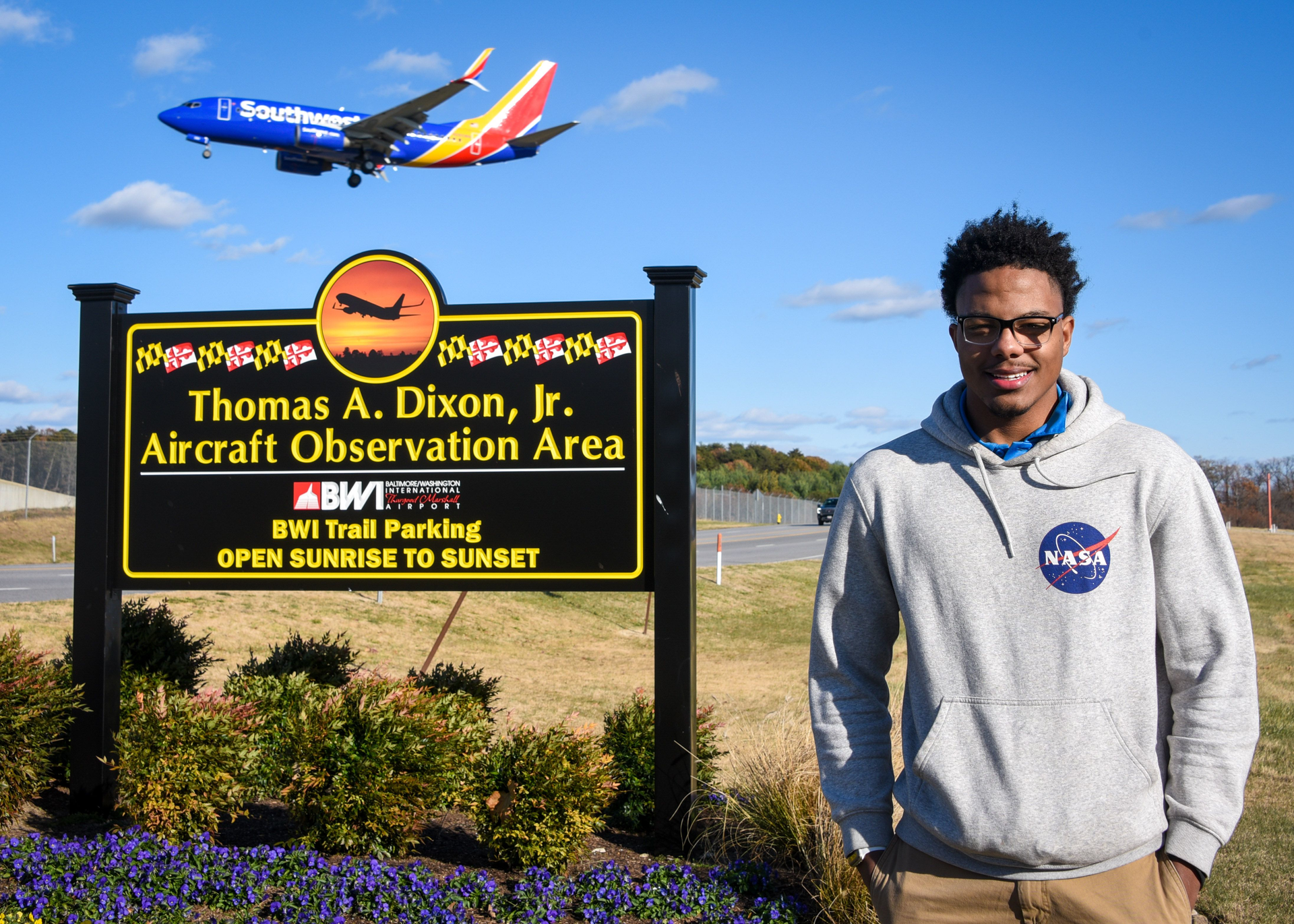 Izaiah Brown, a University of Maryland Eastern Shore aviation science student and aspiring pilot, stands for a portrait Nov. 26, 2021, at the Thomas A. Dixon Jr. Aircraft Observation Center as a Southwest Airlines plane flies behind him.