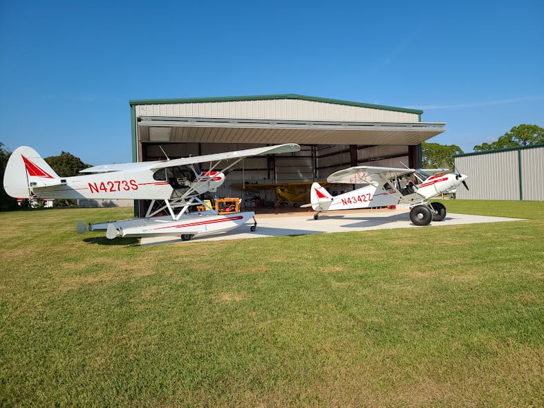 Ray Cook has two hangars with Schweiss Doors bifold liftstrap doors. This hangar at his winter home in Lake Placid, Florida, has a 50 foot by 16-foot, 6-inch Schweiss door. Outside his hangar is his 1968 Piper PA-18-150 Super Cub on Tundra tires; a 1959 Piper PA-18 on floats; and his 1946 Piper J-3 Cub is inside the hangar.