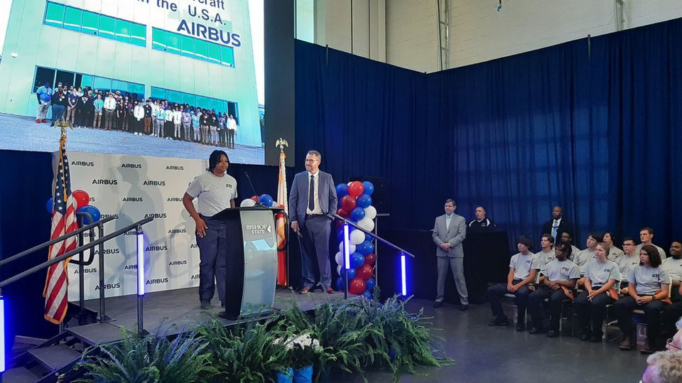 Taking the stage with Airbus executive Daryl Taylor, student trainee Kennedy Brown speaks at a May 9, 2022, event announcing a new Airbus assembly line will be built in Mobile. At right are other students who have participated in the FlightPath9 training program in Mobile