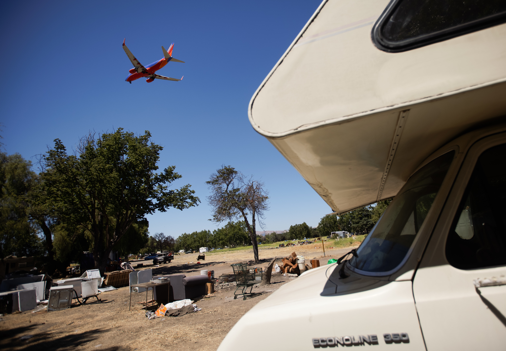 An airplane flies over the homeless encampment located along Coleman Avenue in San Jose, Calif., on Monday, June 28, 2021.
