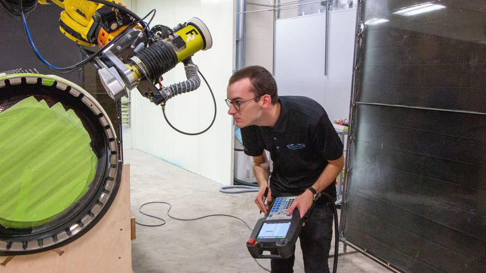 Landon Beachy, process engineer, tests a robot s ability to move closely over a part to be coated.