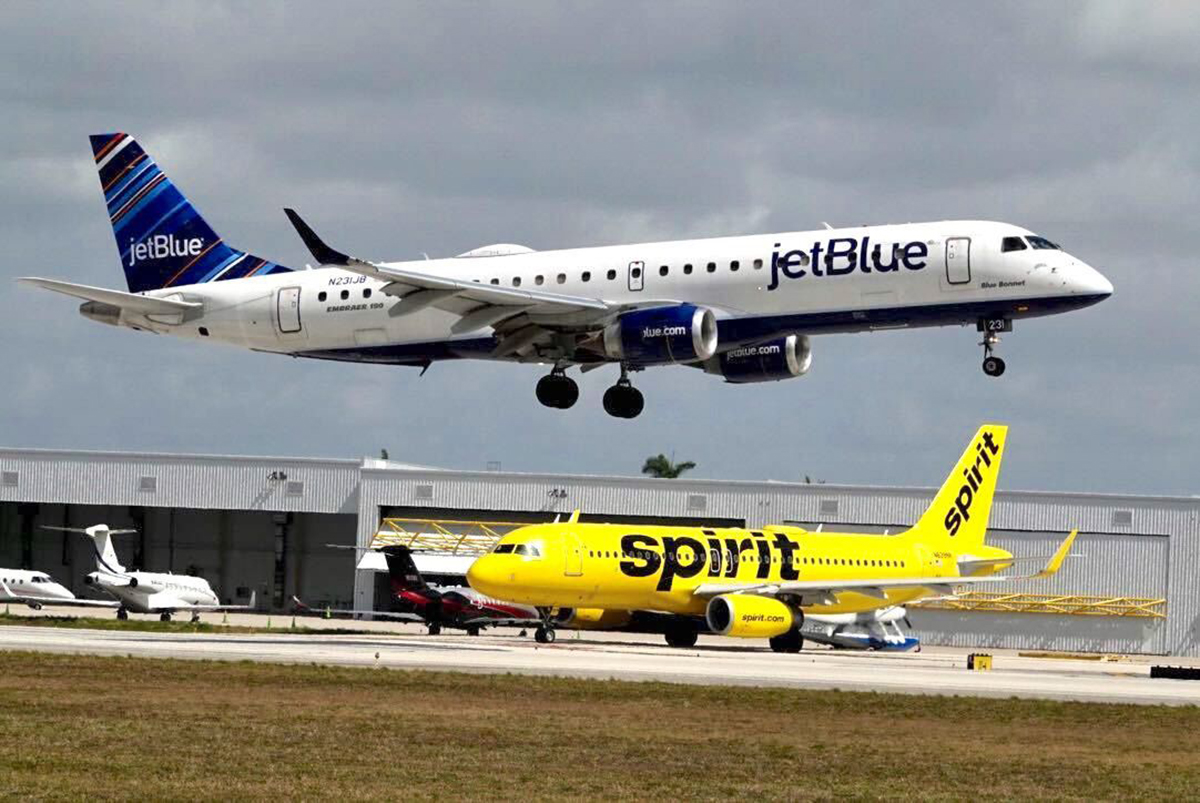 A JetBlue airliner lands past a Spirit Airlines jet on taxi way at Fort Lauderdale Hollywood International Airport on Monday, April 25, 2022.