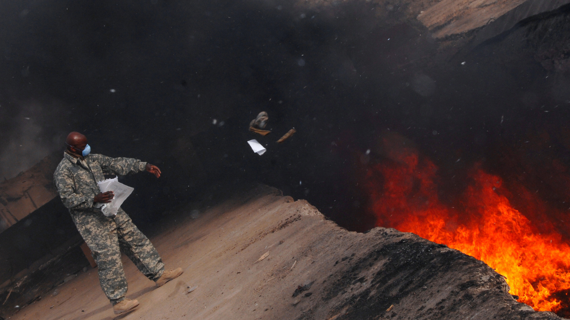 An Air Force service member tosses items into a burn pit at Balad Air Base, Iraq, in March 2008.