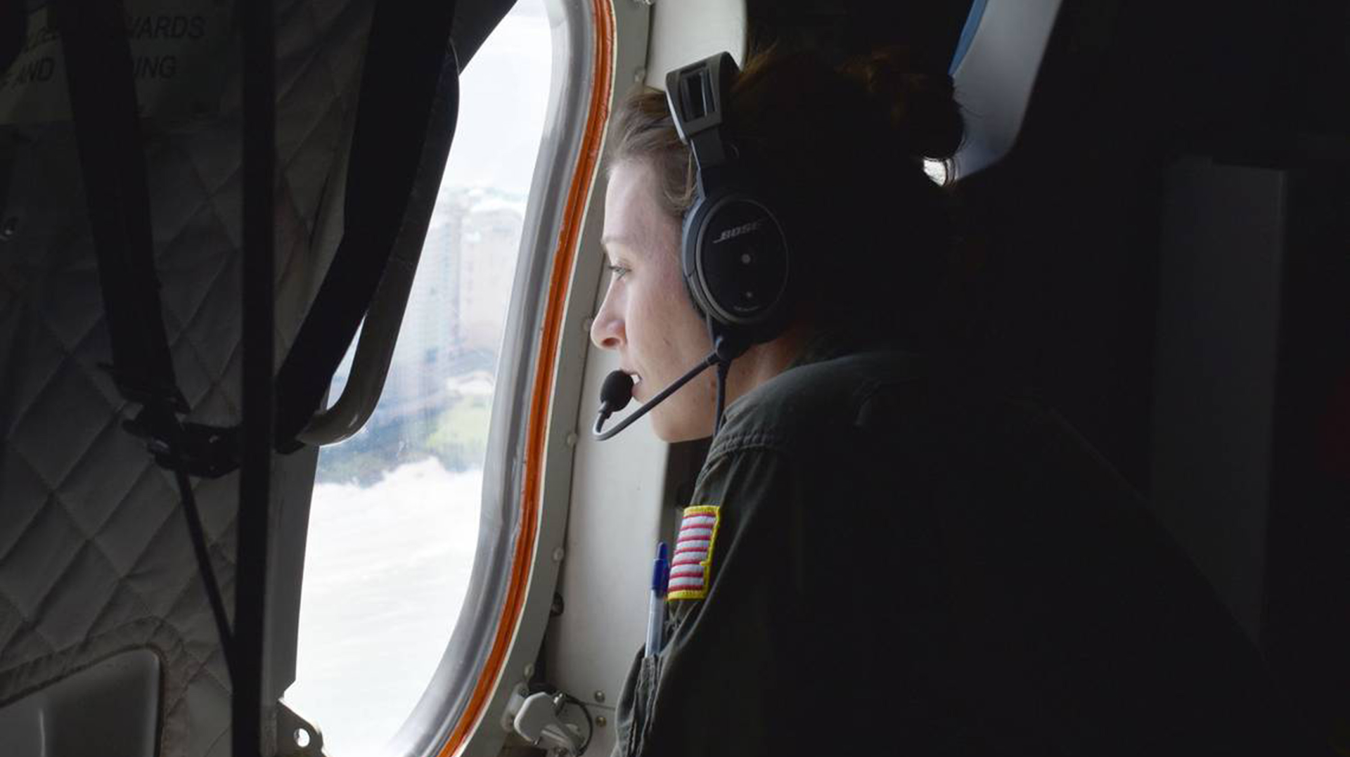 A Coast Guard flight crew member looks out the window as she's positioned to watch for any danger on a flight to Southwest Florida on Sunday, Oct. 2, 2022.