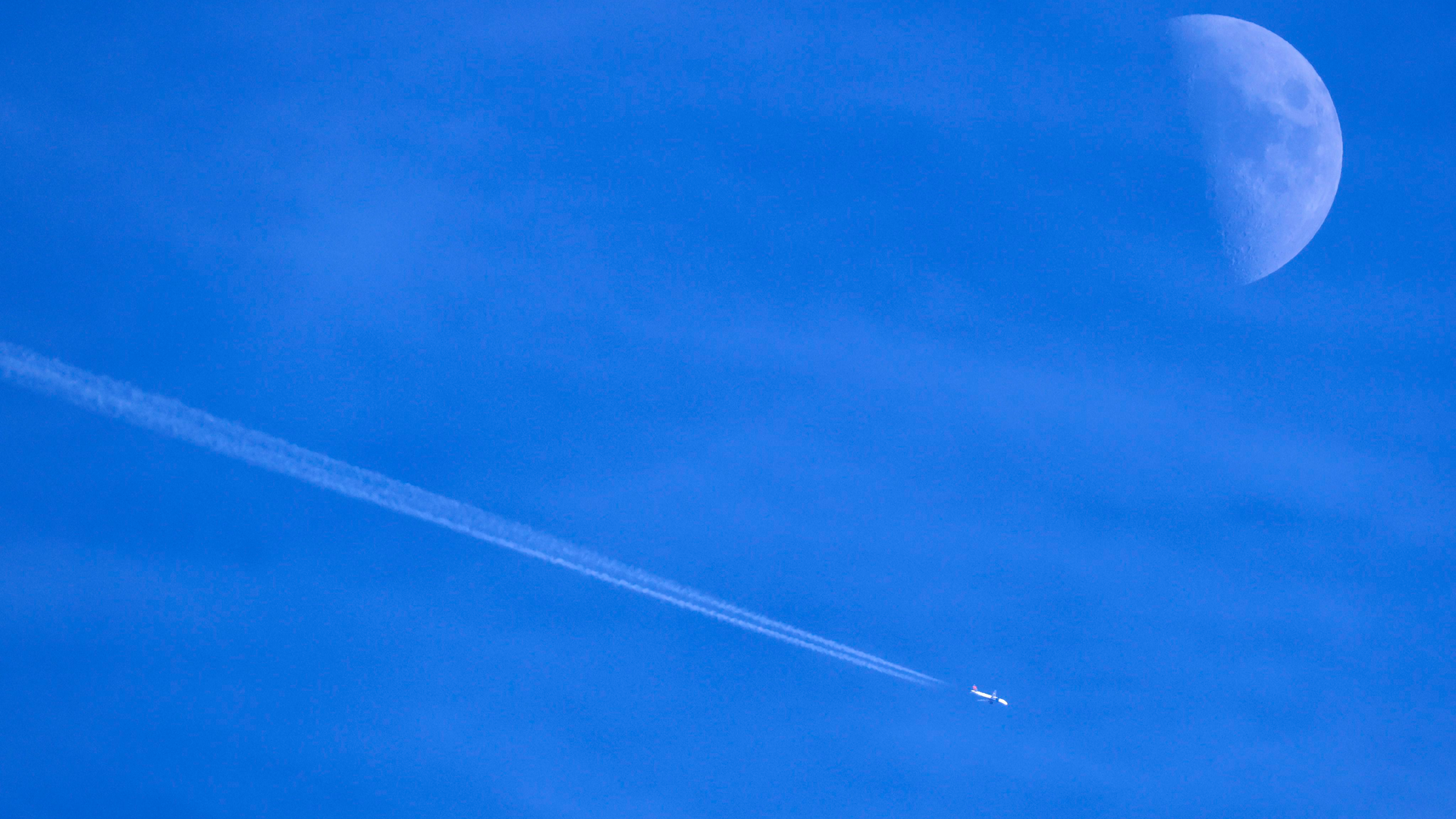 Contrails form behind a commercial jet passing by the moon over Dallas.