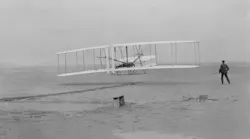 Orville Wright takes off in the first flight of the 1903 flyer as Wilbur Wright assists.