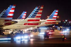 Baggage carts pass American Airlines planes at the gates of Terminal C at Dallas/Fort Worth International Airport.