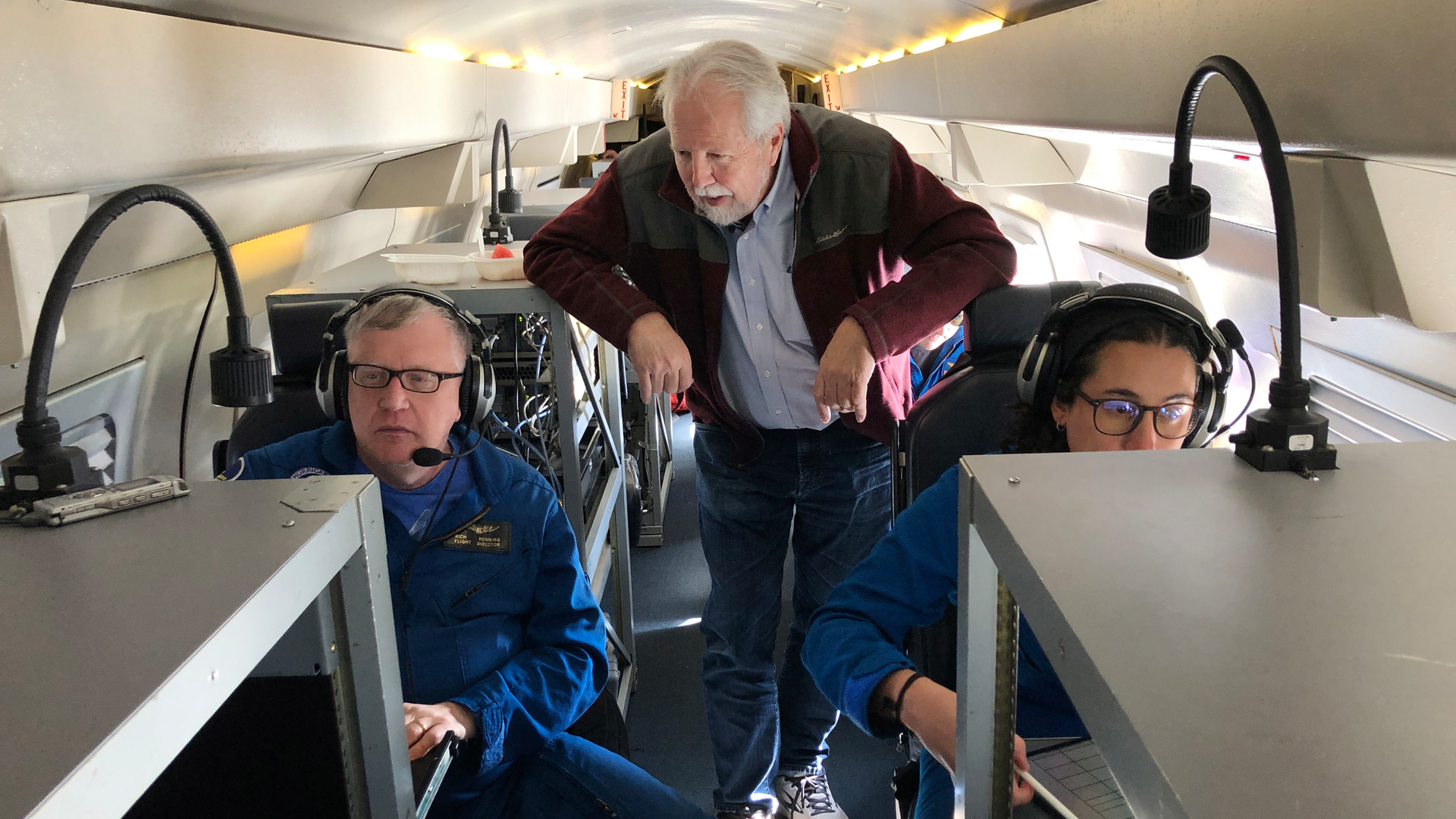 Marty Ralph, center, watches as meteorologists Rich Henning, left, and Sofia de Solo track data while flying above an atmospheric river over the Pacific Ocean.