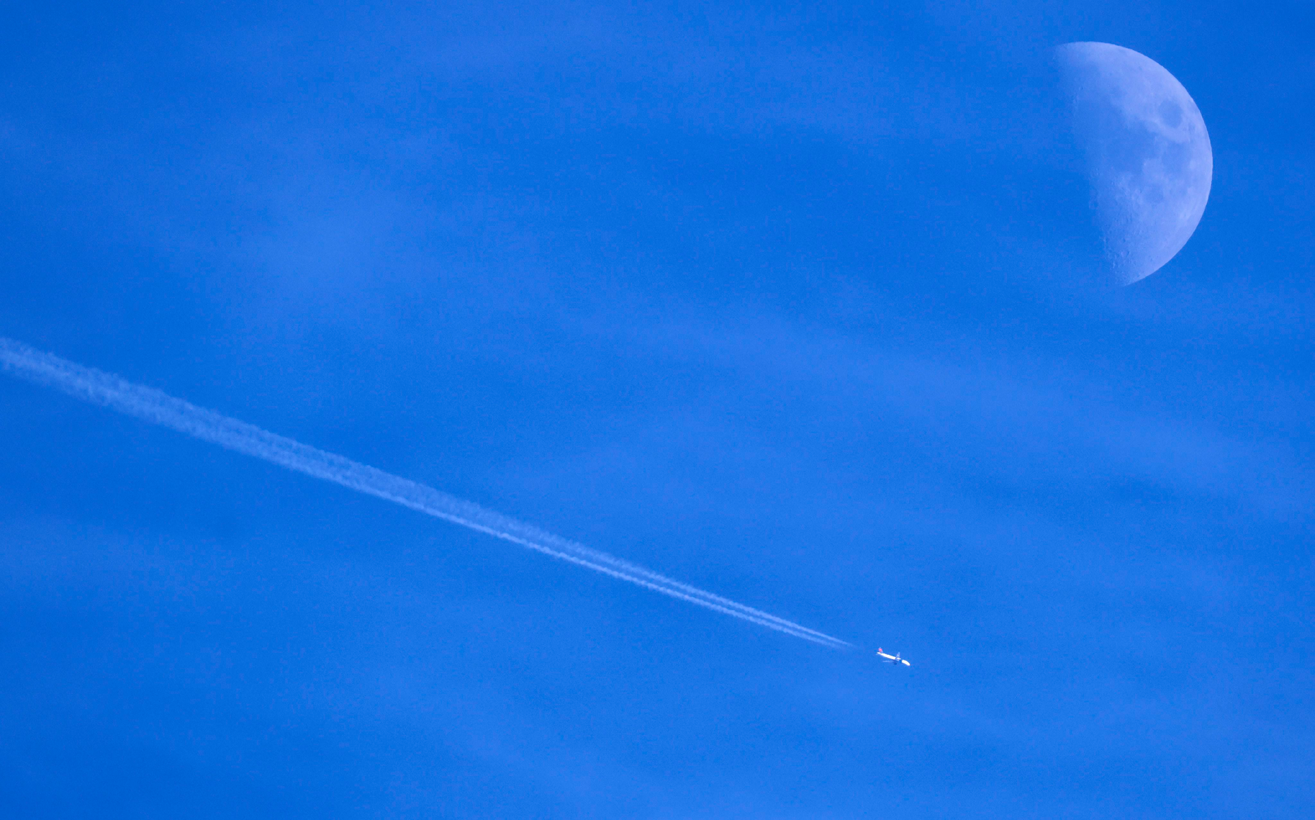 Contrails form behind a commercial jet passing by the moon over Dallas, November 30, 2022.