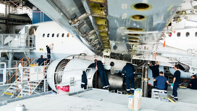 A group of mechanics works on a disassembled airplane in a hangar.