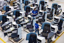 Employees in blue shirts walk between and sit at work stations with computers. Employees in blue shirts walk between and sit at work stations with computers.