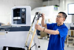 A man in a blue shirt working on a component next to a piece of electronic equipment. A man in a blue shirt working on a component next to a piece of electronic equipment.