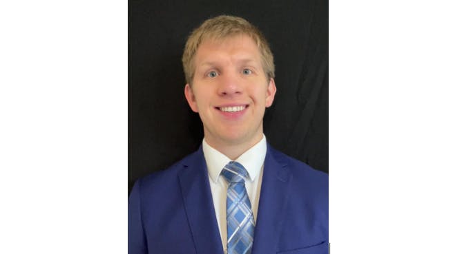 A man in a blue suit and tie smiles at the camera