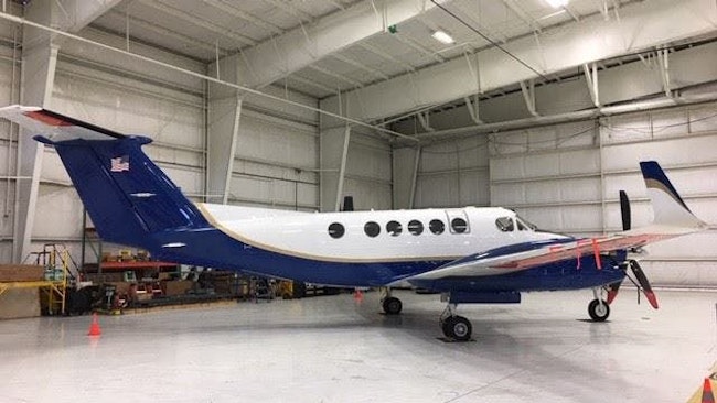 A blue and white airplane sits in a brightly lit airplane hangar
