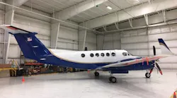 A blue and white airplane sits in a brightly lit airplane hangar