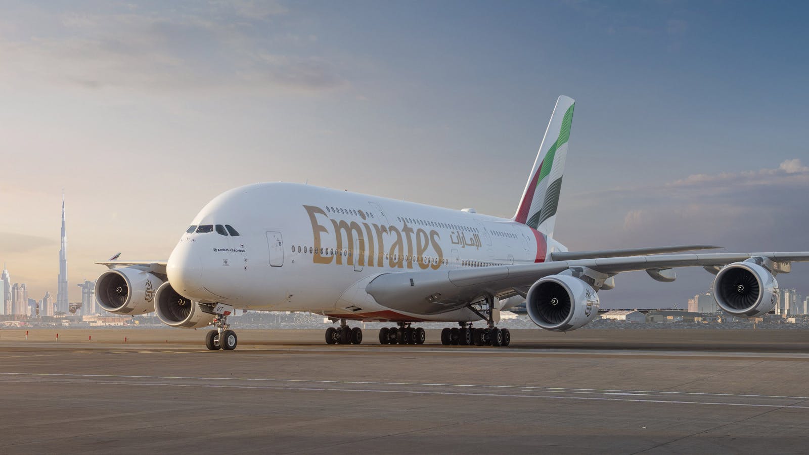 An airplane with the text 'Emirates' on it sits on a tarmac with the sun behind