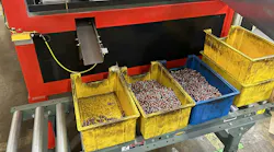 A group of yellow and blue plastic bins filled with coated metal threaded inserts on a conveyor belt