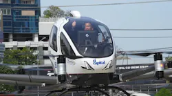 A man gives a thumbs-up from inside a white aircraft that resembles a helicopter
