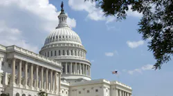 The U.S. Capitol Building with white domes and pillars and an American flag against a blue sky