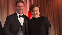 A woman in a black dress stands next to a man wearing a black suit and holding a crystal award, both smiling A woman in a black dress stands next to a man wearing a black suit and holding a crystal award, both smiling