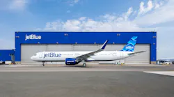 A white airplane with blue accents and text that reads 'JetBlue' sits parked in front of a facility with the label 'JetBlue'