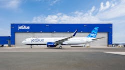 A white airplane with blue accents and text that reads 'JetBlue' sits parked in front of a facility with the label 'JetBlue' A white airplane with blue accents and text that reads 'JetBlue' sits parked in front of a facility with the label 'JetBlue'