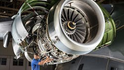 An aircraft maintenance technician in a blue shirt works on a large aircraft engine An aircraft maintenance technician in a blue shirt works on a large aircraft engine