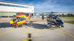 A yellow helicopter and a black helicopter sit in front of a white building