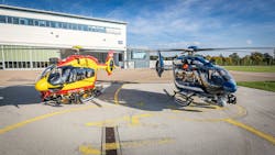 A yellow helicopter and a black helicopter sit in front of a white building A yellow helicopter and a black helicopter sit in front of a white building