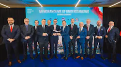 A group of professionals in business attire stand smiling in front of a banner that reads 'Memorandums of Understanding Signing Ceremony'