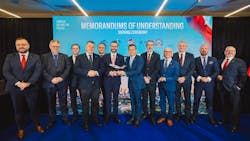 A group of professionals in business attire stand smiling in front of a banner that reads 'Memorandums of Understanding Signing Ceremony' A group of professionals in business attire stand smiling in front of a banner that reads 'Memorandums of Understanding Signing Ceremony'