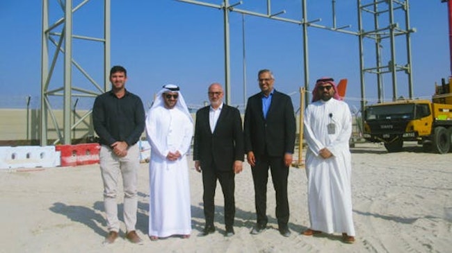 Five men in professional attire stand smiling at the camera on a construction site, with metal framework of a building behind them