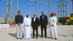 Five men in professional attire stand smiling at the camera on a construction site, with metal framework of a building behind them Five men in professional attire stand smiling at the camera on a construction site, with metal framework of a building behind them