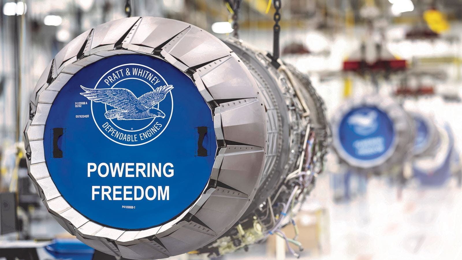 A close-up shot of an airplane engine with a blue graphic in front that reads, 'Pratt & Whitney Dependable Engines Powering Freedom'