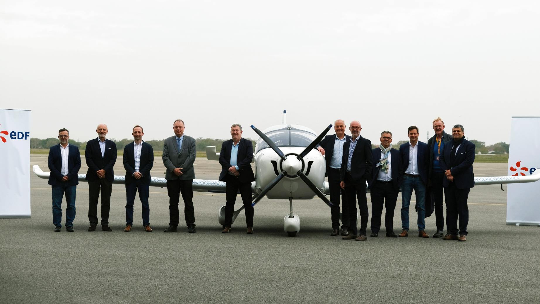 A group of professionals in suits stands in front of an airplane between two signs that read 'EDF'