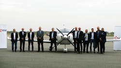 A group of professionals in suits stands in front of an airplane between two signs that read 'EDF' A group of professionals in suits stands in front of an airplane between two signs that read 'EDF'