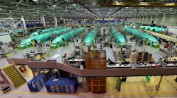 An aircraft hangar shows a row of green airplanes behind an assembly line