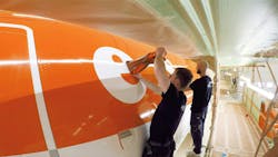 Two technicians wearing black clothing painting an orange and white airplane Two technicians wearing black clothing painting an orange and white airplane