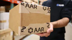 A person in a black shirt that says 'AAR' on it holding a brown shipping box with 'AAR' written on it in the same font
