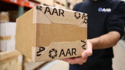 A person in a black shirt that says 'AAR' on it holding a brown shipping box with 'AAR' written on it in the same font A person in a black shirt that says 'AAR' on it holding a brown shipping box with 'AAR' written on it in the same font