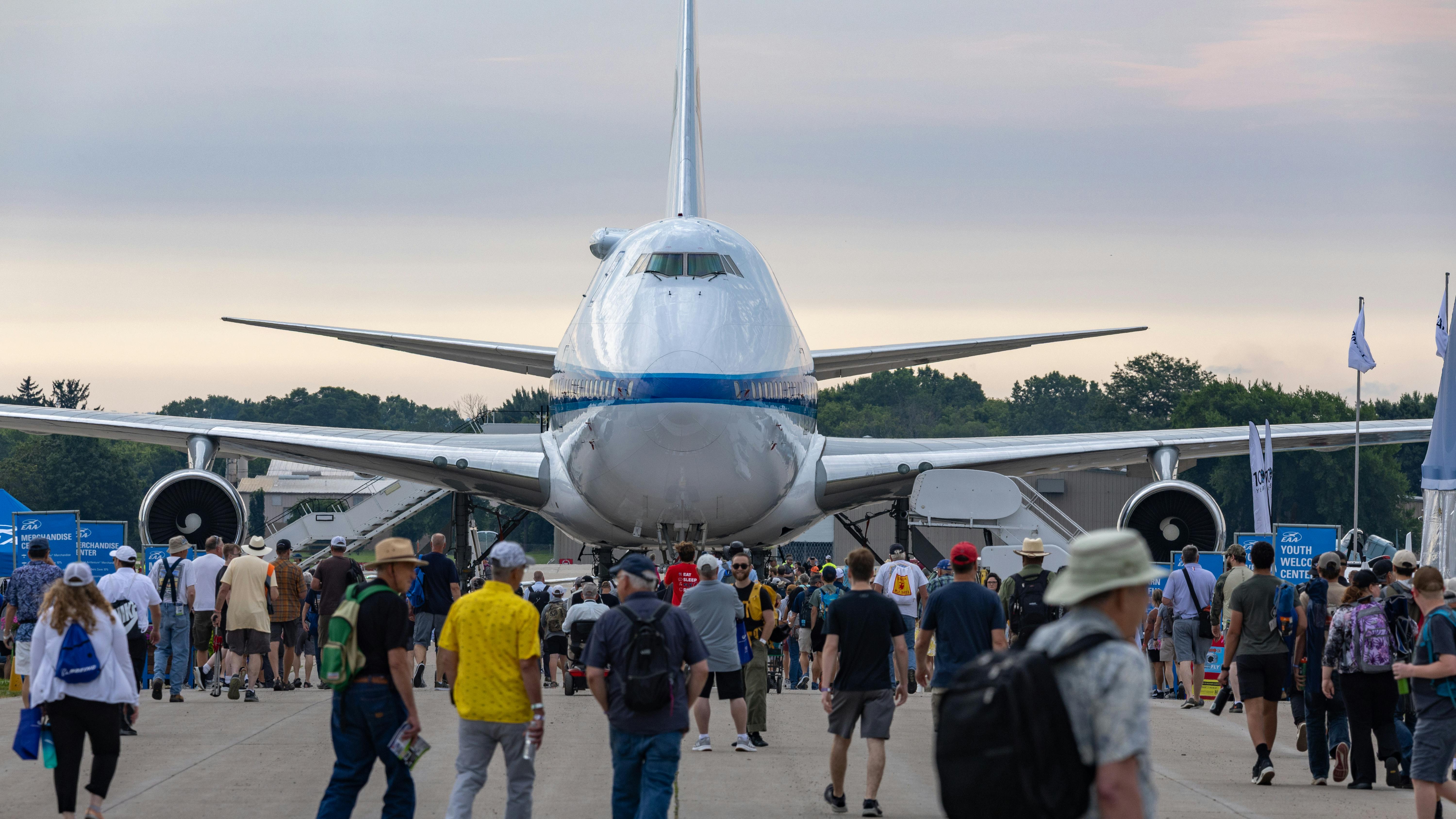 A large airplane sits on pavement surrounded by people walking on the ground around it